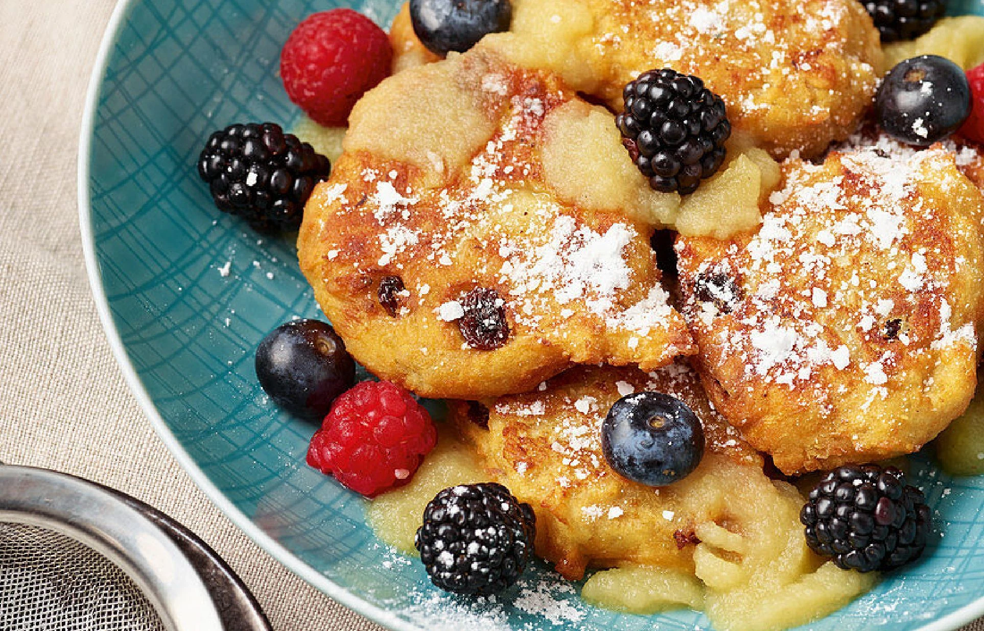Ein Teller mit Vanille-Quarkkäulchen mit Blaubeeren, schwarzen Johannisbeeren und Puderzucker